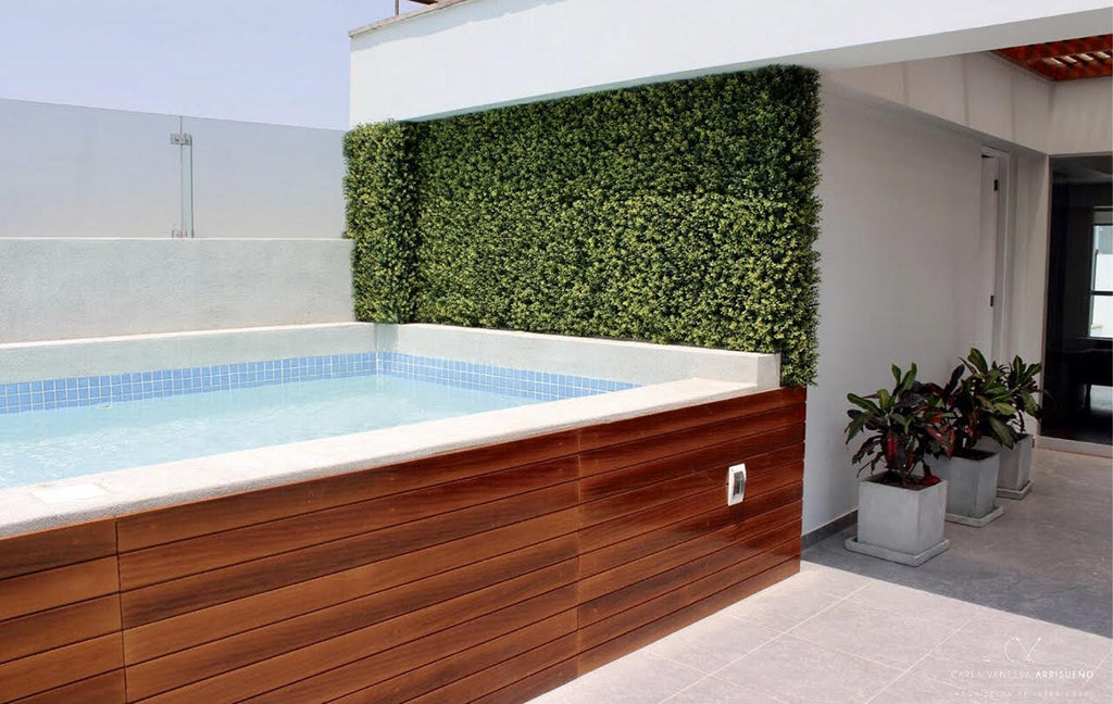 Foto de una terraza. Hay una piscina elevada sobre el nivel del suelo. Su exterior es de madera. Atrás de la piscina hay una pared cubierta con plantas.