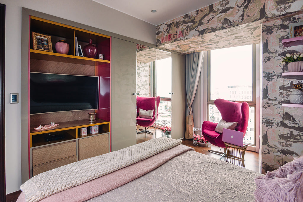 Foto de un cuarto. Hay una cama doble, un sillón pequeño color rosado, y un mueble con una televisión.